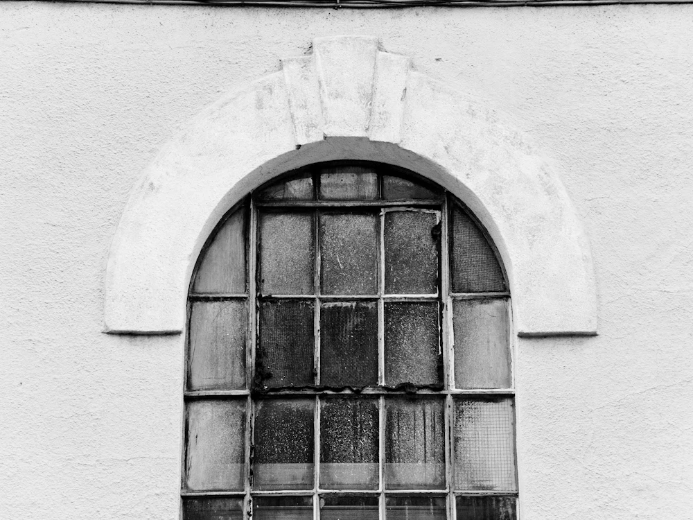 Altes Stahlfenster mit Rundbogen in einer hellen Wand.